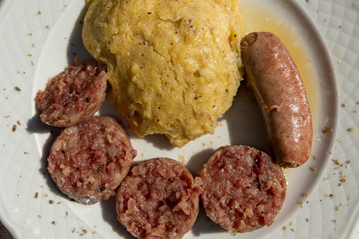 Close up view, directly above the surface, of a traditional plate of the Friuli Venezia Giulia region, made with a sausage, cornmeal mush and slices of pork meat