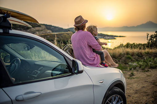 Photo of a boy and his mother on a road trip by the seaside, enjoys together in great sunrise.
