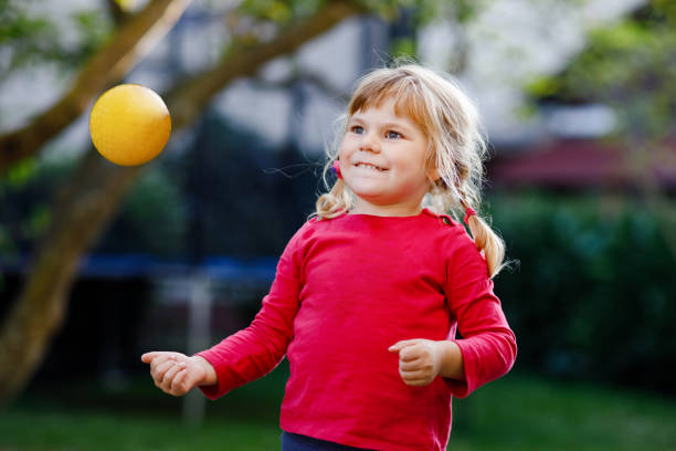 Little adorable toddler girl playing with ball outdoors. Happy smiling child catching and throwing, laughing and making sports. Active leisure with children and kids. stock photo