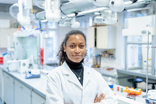 Portrait of female scientist in laboratory. Confident african scientist wearing lab coat standing with arms crossed.