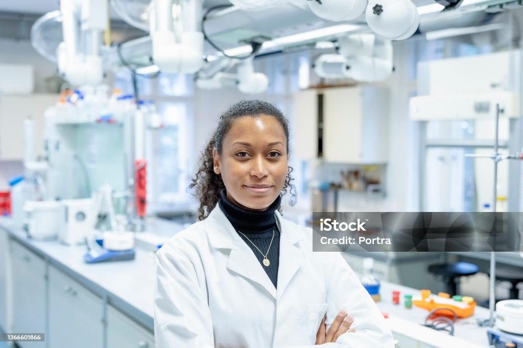 Portrait of confident woman scientist in laboratory Portrait of female scientist in laboratory. Confident african scientist wearing lab coat standing with arms crossed. Laboratory Stock Photo