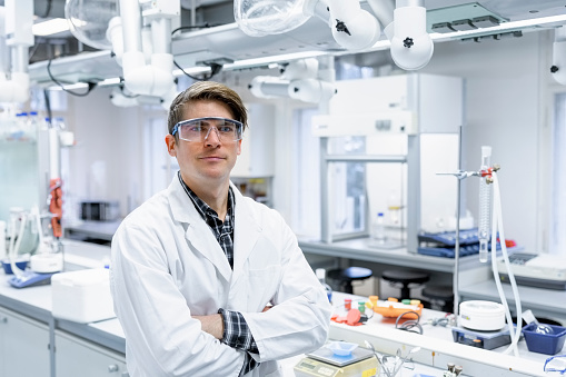 Portrait of confident male researcher standing with arms crossed. Male scientist wearing lab coat in chemistry laboratory.