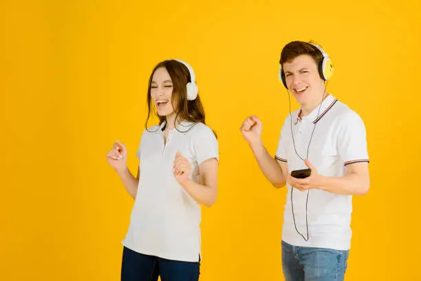 Photo of Portrait of a young happy couple man and woman listening to music in headphones and laughing on a yellow background.