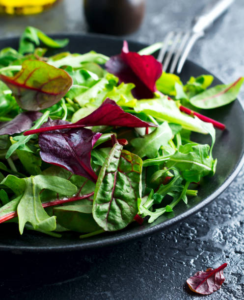 Mix fresh leaves of arugula, lettuce, spinach, beets for salad on a dark stone background. Selective focus. stock photo