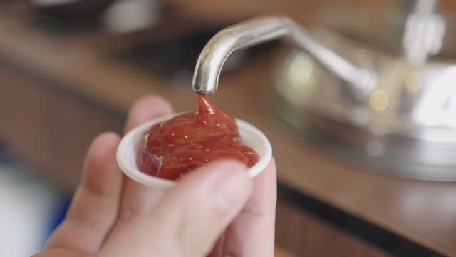 Man's hand pumping ketchup into plastic cup.