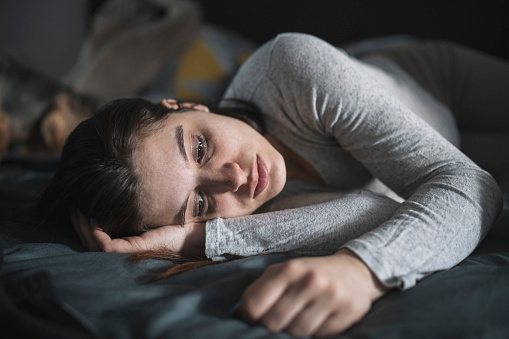 Depressed young woman laying and crying in bed.