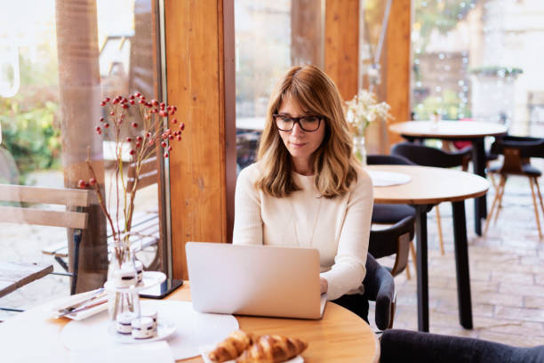 istock Smiling mature woman using laptop and working while sitting at the cafe 1366614485