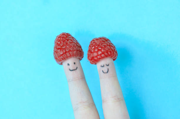 istock Two fingers with smiles and raspberry as a hat. Blue background. 1366618137
