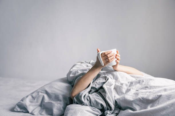istock A woman's hand holds a cup of coffee while lying in bed. 1366618199