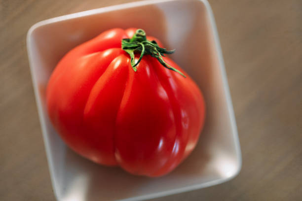 Juicy tomato in white bowl, close-up