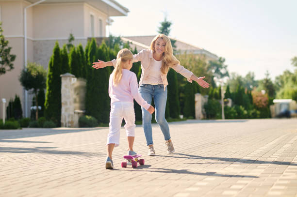 istock Blonde woman helping her daughter learn skateboarding 1366619537