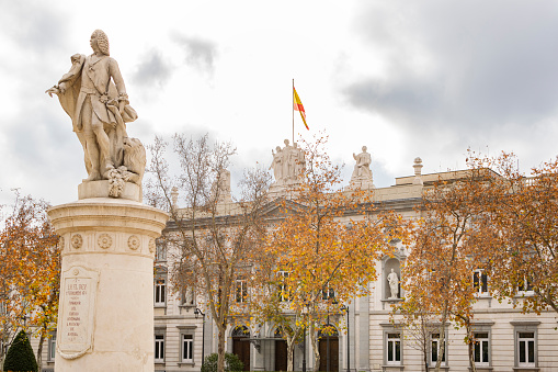 Madrid, Spain - December 19, 2021:Gardens of the Plaza Villa de Paris with the Statue of Fernando VI built by Juan Domingo Olivieri in 1752, and the supreme court building in the background in Madrid, Spain.