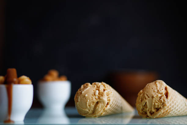 istock two caramel ice cream in waffle cones on a white glass surface on a black background, next to white coffee cups with caramel candies 1366622632