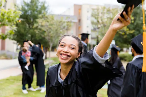 Photo of Excited young adult graduate raises cap in hand