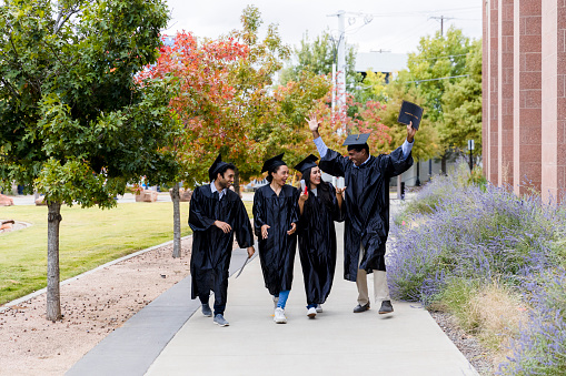 After the graduation ceremony, the adult college graduates smile and talk together as they walk.
