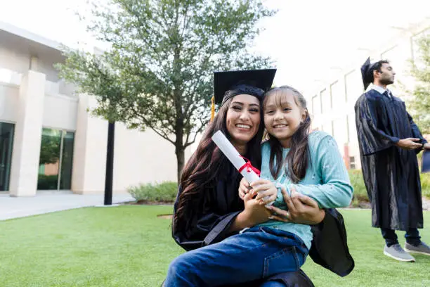 The young adult female graduate poses with her diploma and her elementary age niece.