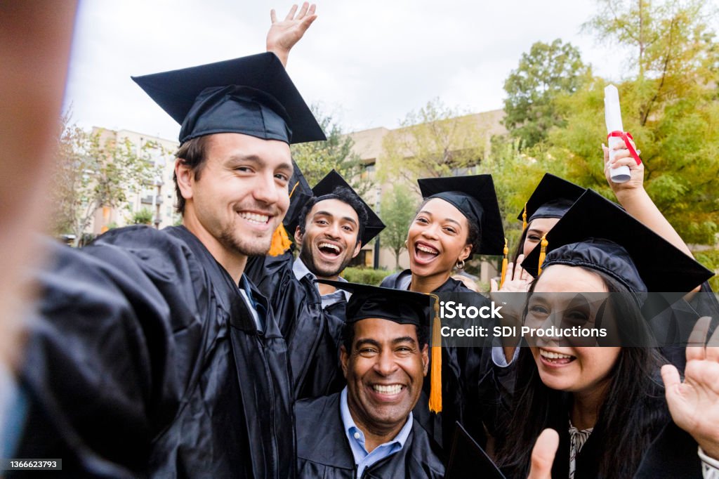 Diverse friends group takes joyful photo after graduation The diverse group of friends takes a selfie as they smile and cheer after the graduation ceremony. Graduation Stock Photo
