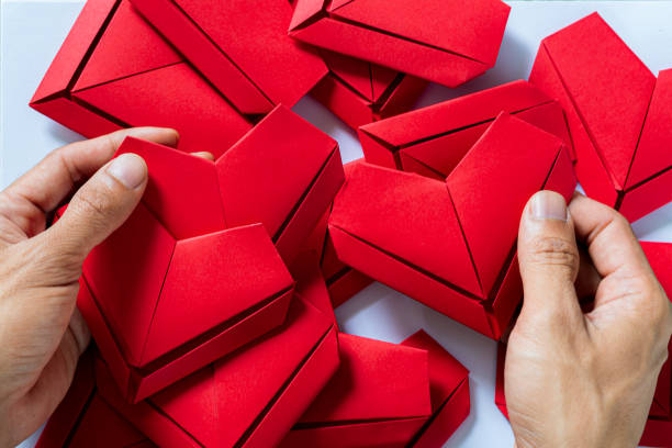 corazón de papel, manos que sostienen el fondo blanco del corazón de origami doblado, la mano del niño que sostiene el papel del corazón rojo sobre fondo azul - possing love passion romance fotografías e imágenes de stock