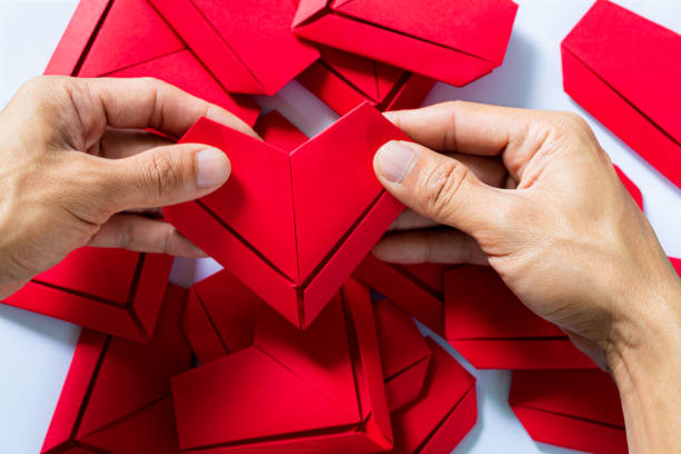 corazón de papel, manos que sostienen el fondo blanco del corazón de origami doblado, la mano del niño que sostiene el papel del corazón rojo sobre fondo azul - possing love passion romance fotografías e imágenes de stock