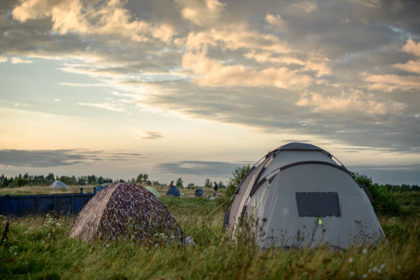 Camping tents are neatly pitched on rocky terrain by the lake. The early morning mist in the distant Sahyadri mountains, casting a calming blue hue over the scene. The peaceful setup captures the essence of outdoor adventure and nature's stillness in this remote Maharashtra hideaway.