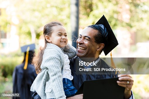 istock Little girl makes graduating grandfather laugh with silly face 1366624112