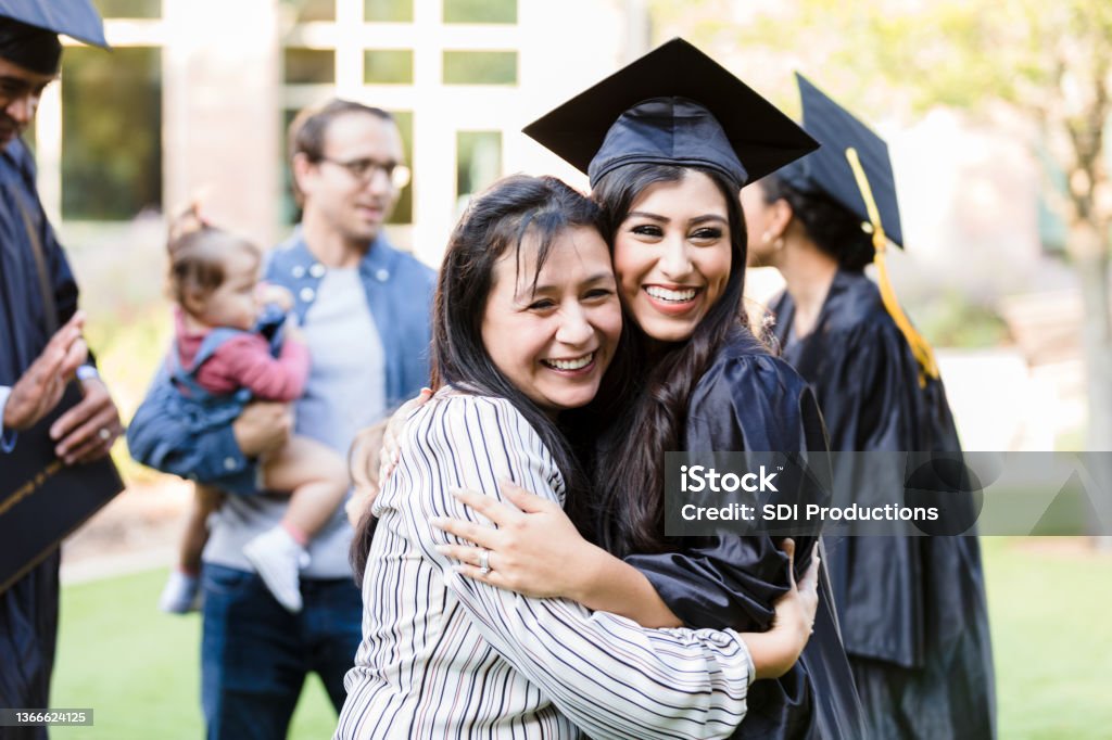 Mother and graduating daughter pose cheek to cheek for photo A mid adult mother and her young adult graduating daughter pose cheek to cheek with big smiles for a photo taken by an unseen person. Graduation Stock Photo
