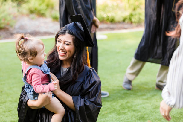 mom in cap and gown laughs with baby daughter - life events laughing women latin american and hispanic ethnicity imagens e fotografias de stock