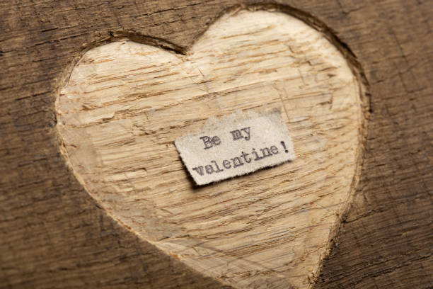istock Be my Valentine - tiny typed text note close up. Valentines Day greetings concept. Carved heart shape on wood as background for Valentines greeting card. 1366624163