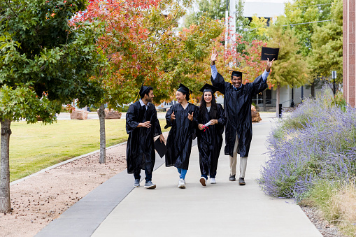 After their college graduation, a group of diverse college graduates walk together on campus.