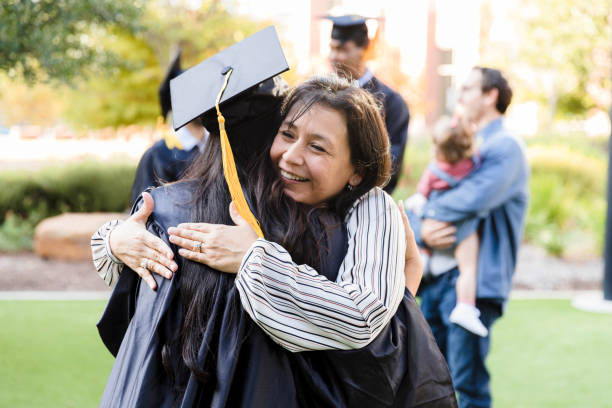 Proud mother hugs unrecognizable daughter after graduation ceremony The proud mid adult mom embraces her unrecognizable young adult daughter after the graduation ceremony. college student and parent stock pictures, royalty-free photos & images