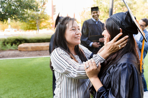 The mid adult mother holds her young adult daughter's head in her hands as she tells her daughter how proud she is on her daughter's graduation day.