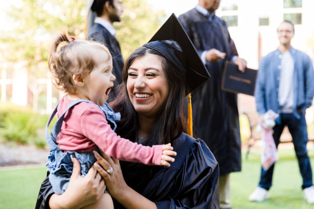 Mother in cap and gown smiles at cute baby daughter