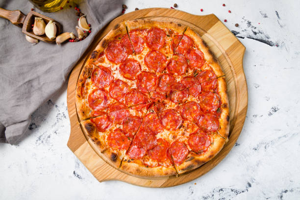 istock Pepperoni pizza on wooden board on grey table top view 1366624476