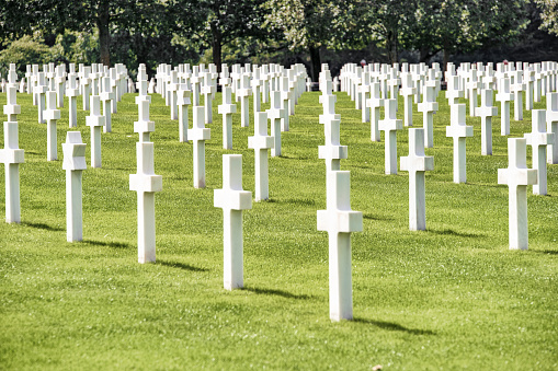 Colleville-sur-Mer, Normandy, France, September 03, 2019: Looking at the Normandy American Cemetery and Memorial (French: Cimetière américain de Colleville-sur-Mer). It is a World War II cemetery and memorial in Colleville-sur-Mer, Normandy, France, that honors American troops who died in Europe during World War II. It is located on the site of the former temporary battlefield cemetery of Saint Laurent, covers 172.5 acres and contains 9,388 burials.\nThe cemetery, which was dedicated in 1956, is the most visited cemetery run by the American Battle Monuments Commission (ABMC) with over one million visitors a year.