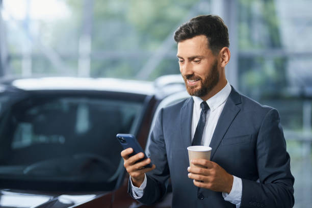 Businessman using smartphone while buying new car at salon stock photo