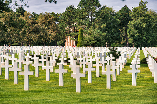Colleville-sur-Mer, Normandy, France, September 03, 2019: Looking at the Normandy American Cemetery and Memorial (French: Cimetière américain de Colleville-sur-Mer). It is a World War II cemetery and memorial in Colleville-sur-Mer, Normandy, France, that honors American troops who died in Europe during World War II. It is located on the site of the former temporary battlefield cemetery of Saint Laurent, covers 172.5 acres and contains 9,388 burials.\nThe cemetery, which was dedicated in 1956, is the most visited cemetery run by the American Battle Monuments Commission (ABMC) with over one million visitors a year.