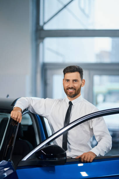 istock Businessman standing at auto salon and smiling on camera 1366626948