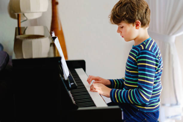 リビングルームでピアノを弾く美しい小さな子供の男の子。子供はタブレットアプリで楽器を演奏することを学んで楽しんでいます。ホームスクーリングコロナウイルスロックダウン中のeラ - piano keyboard instrument one person piano key ストックフォトと画像
