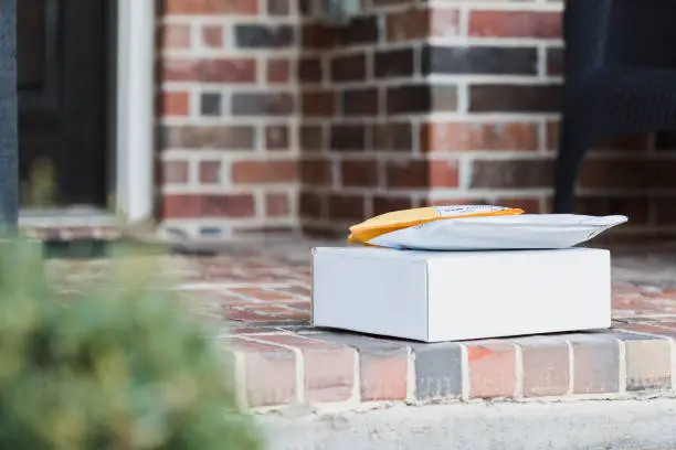A close up photo of a white cardboard box and two envelopes on front porch of home ready for pick-up by mail person or home owner.