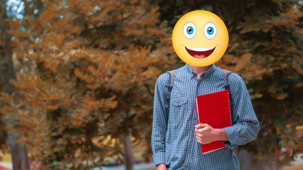 University student posing for the camera outdoors. The person whose identity is unknown has a smiley face emoji on their head.