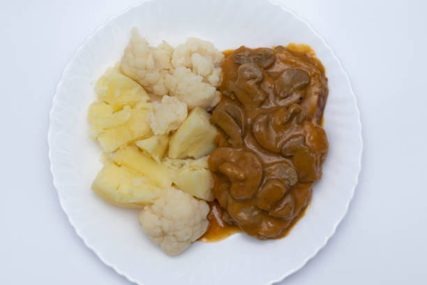 A meat dish with mushroom sauce, accompanied by potatoes with cauliflower. Isolated on white background. Delicious food concept.