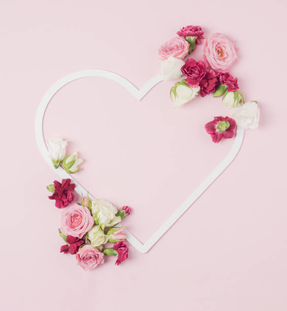 istock Heart shaped frame with colorful spring flowers spilled around it on a pastel pink background. 1366633271
