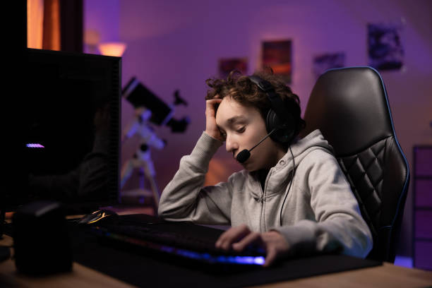 A little boy is upset about losing in a computer game, he lives in a virtual world with a team he talks to through a headset, a child supports head with his hand in sadness of losing a video round