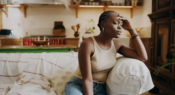 Photo of Shot of an attractive young woman sitting alone on the sofa at home and feeling stressed