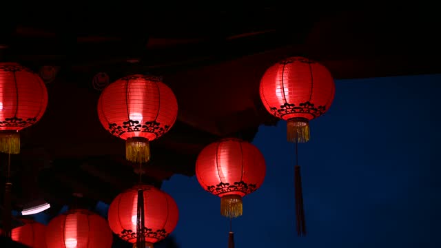 Round red lantern hanging on old traditional temple at night.