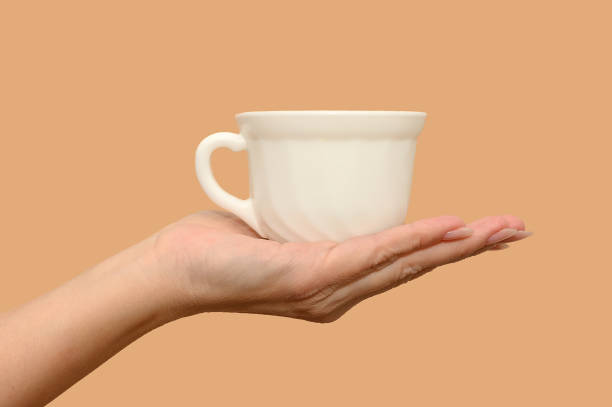 istock A female hand holds a white cup. Minimalism. Close-up. On a beige background. 1366640385