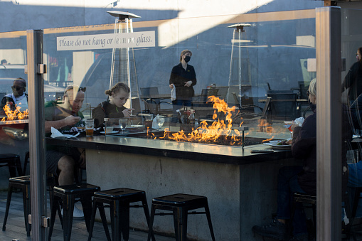 Seaside, OR, USA - Jan 22, 2022: Social distanced people eating in an outdoor setting separated from the streets with glass screens at Finns Fireside Patio, a local seafood restaurant in Seaside, Oregon, amid the Omicron variant surge.