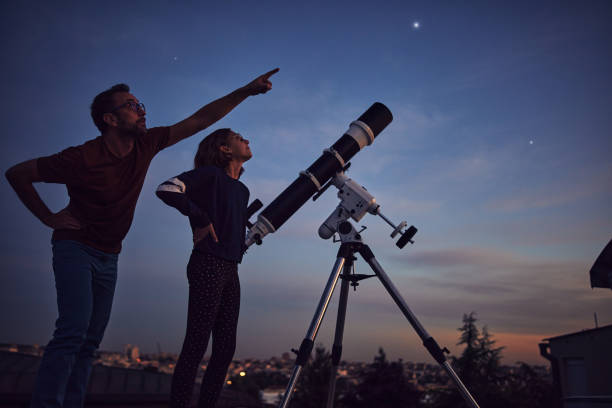 sagome di padre, figlia e telescopio astronomico sotto cieli stellati. - astronomy foto e immagini stock