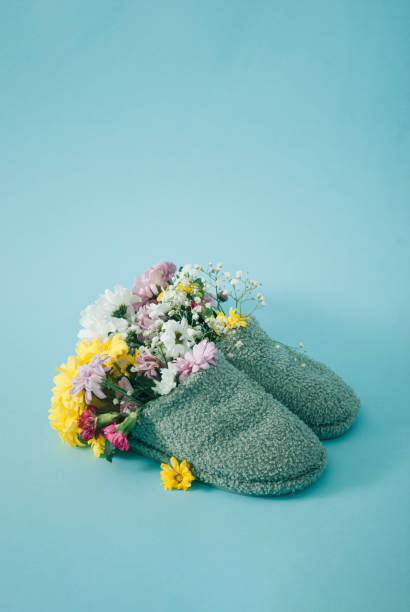 Spring colorful flowers growth from slippers on turquoise background. Creative concept, side view.