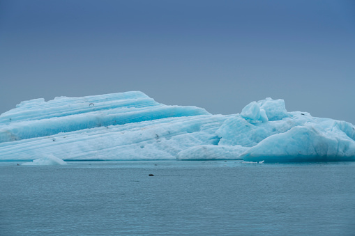 a blue, small expedition ship lies in front of an Antarctic iceberg landscape in Cierva Cove - a deep inlet on the west side of the Antarctic Peninsula, surrounded by rugged mountains and dramatic glacier fronts.